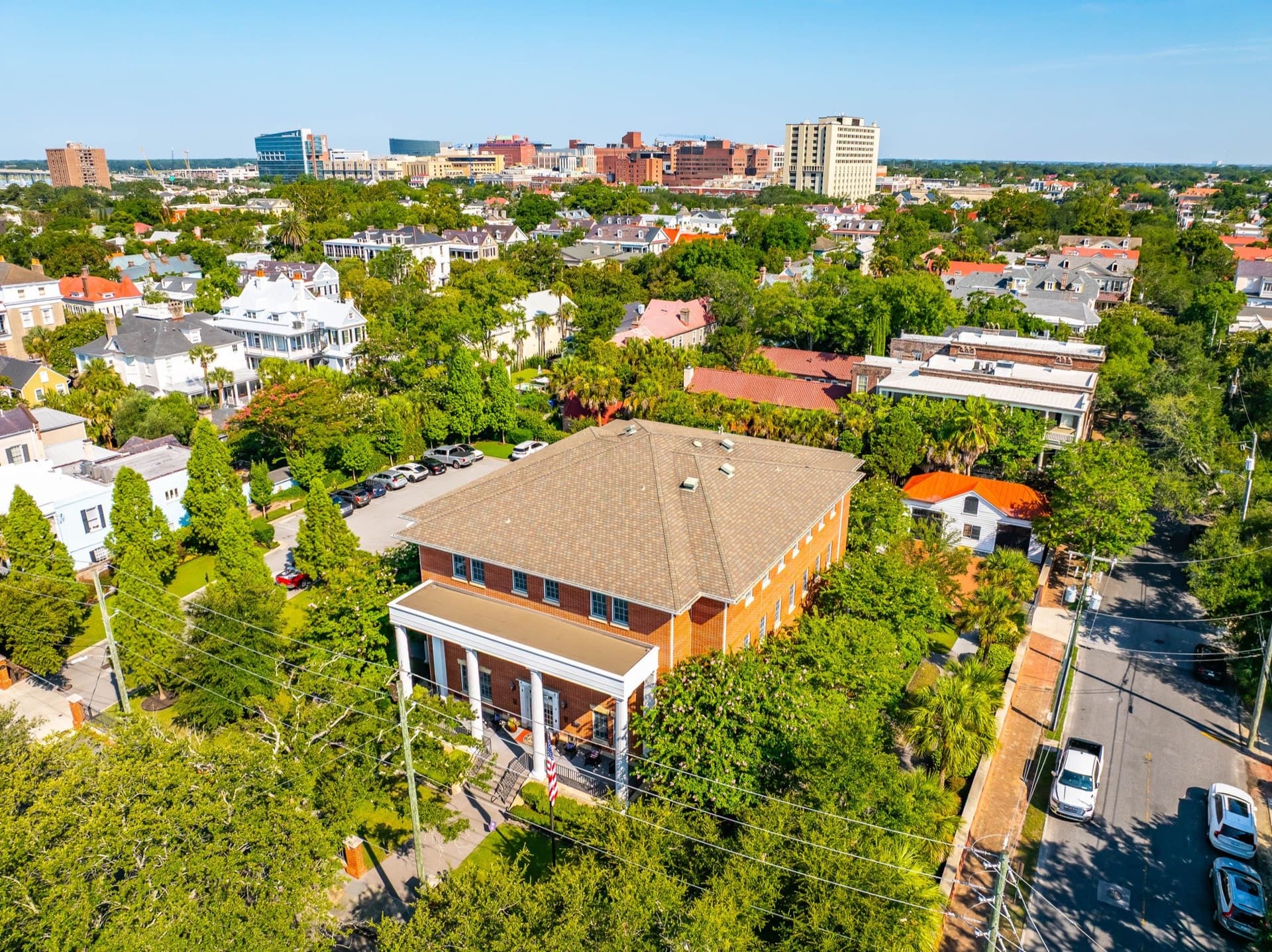 Aerial view of the Charleston Fisher House and its tree-lined neighborhood, with the downtown Charleston medical district skyline in the background.