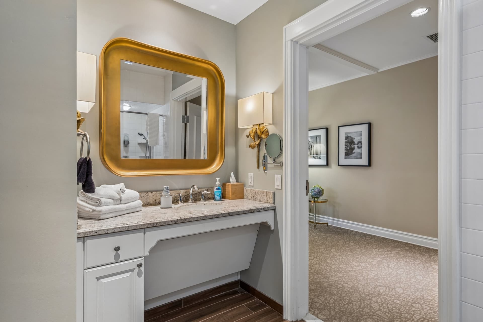 Suite bathroom vanity with a gold-framed mirror, granite counter, and fresh towels, with roll-under sink clearance.