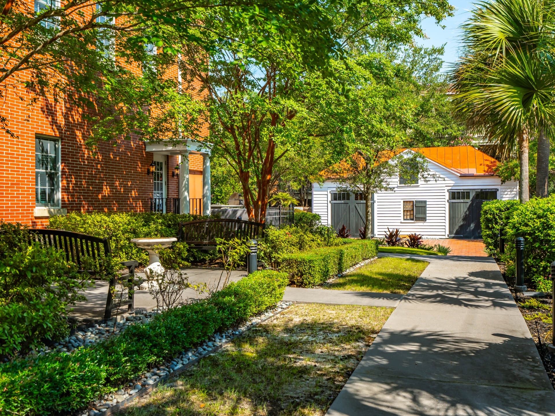 Brick garden pathway beside the Fisher House, lined with benches and landscaping, leading toward a white carriage house.