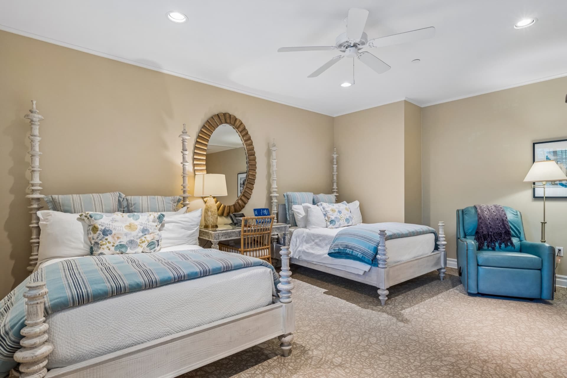 Guest suite with two beds in blue and white linens, a round mirror, writing desk, and leather recliner.