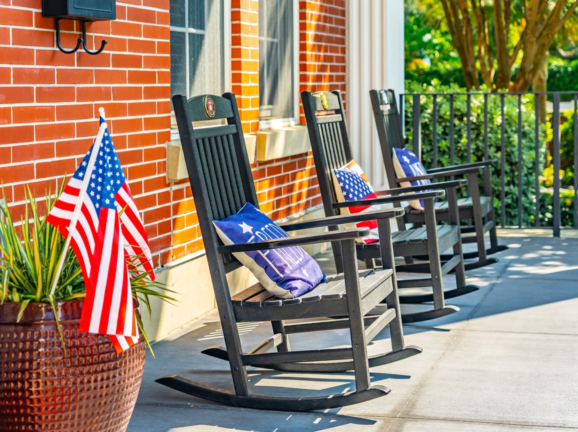 Black rocking chairs with military service branch medallions and American flags on the brick front porch of the Fisher House.