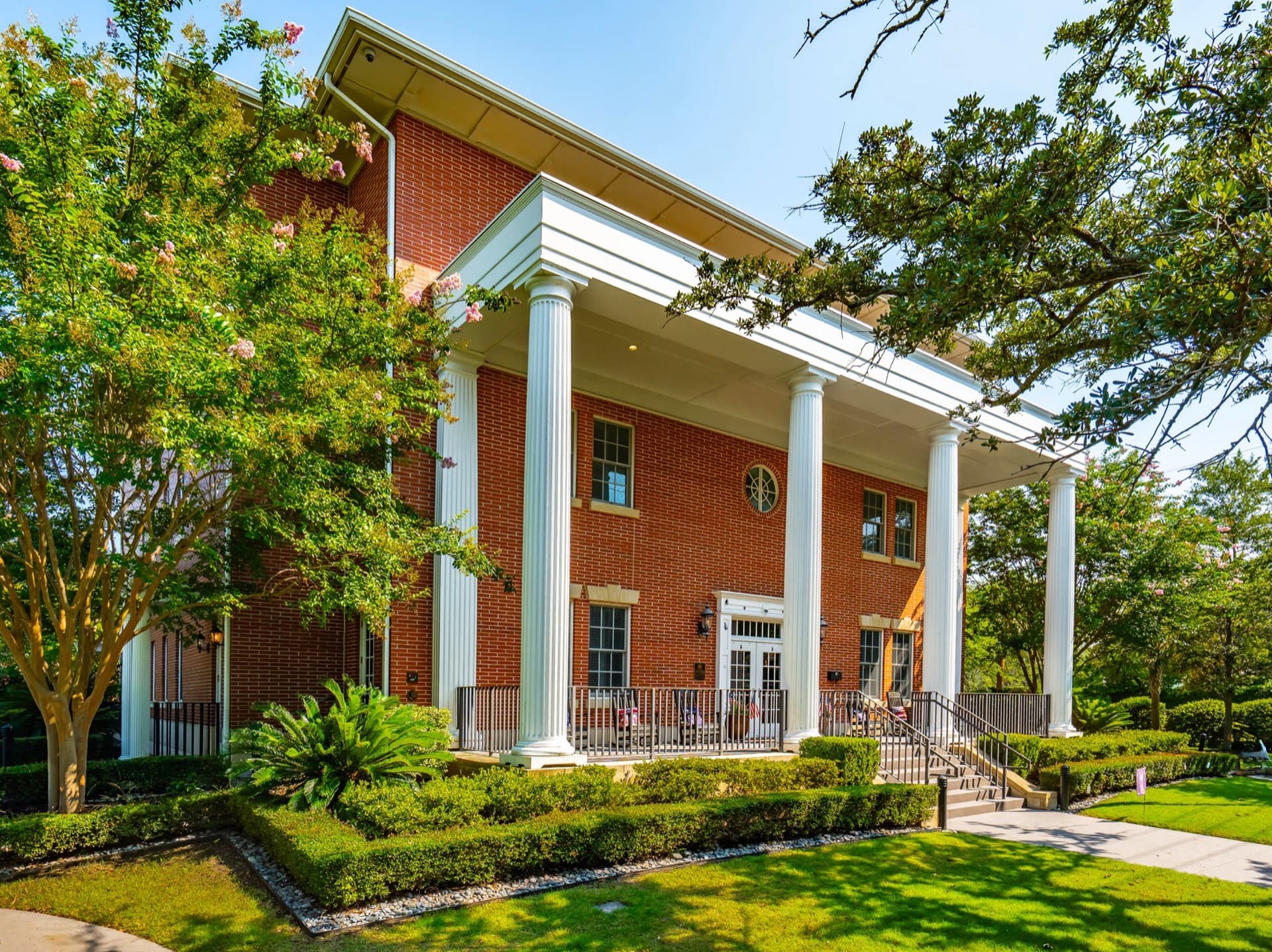 Side porch of the Charleston Fisher House, red brick with two-story white columns and a landscaped garden, framed by a live oak tree.