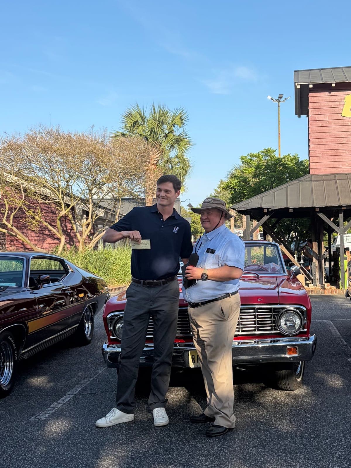 Two men presenting a check in front of a classic red truck at Bessinger's Barbeque during the antique car show