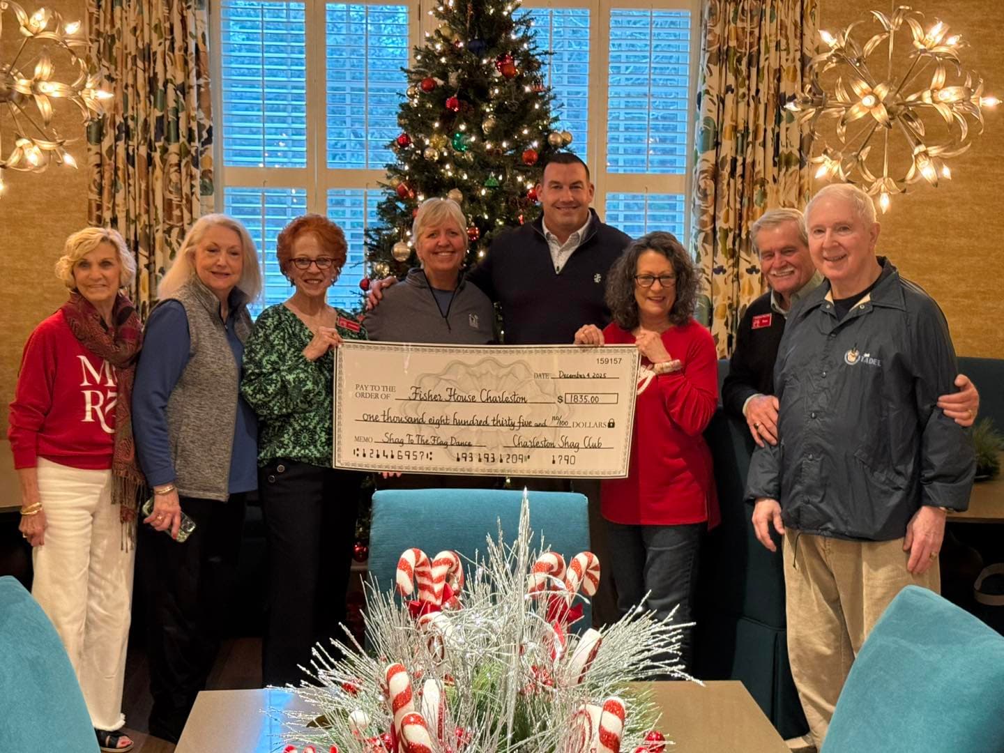 Charleston Shag Club members and Fisher House staff holding a $1,835 check inside the Fisher House living room decorated for Christmas