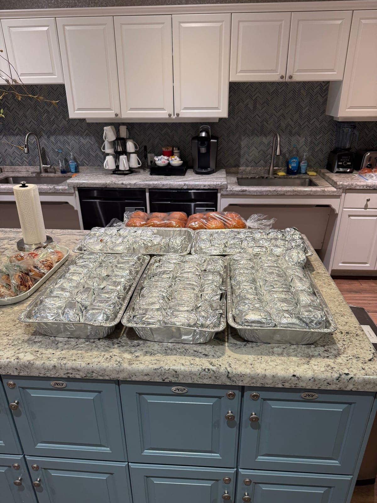 Foil-wrapped trays of pulled pork and brisket sandwiches lined up on the Fisher House kitchen island