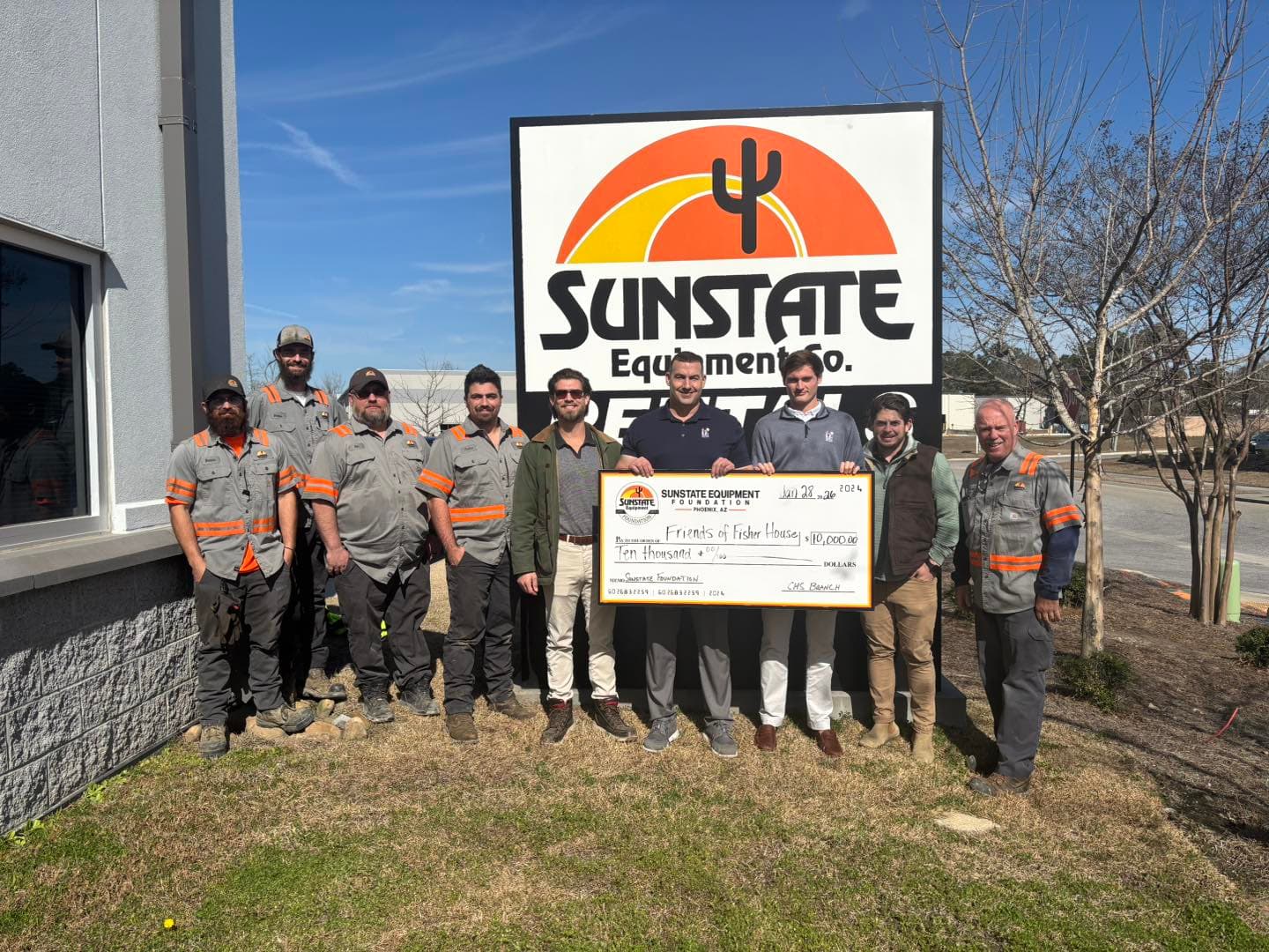 Sunstate Equipment team members and Friends of Fisher House staff holding a $10,000 check in front of the Sunstate Equipment Co. sign in North Charleston